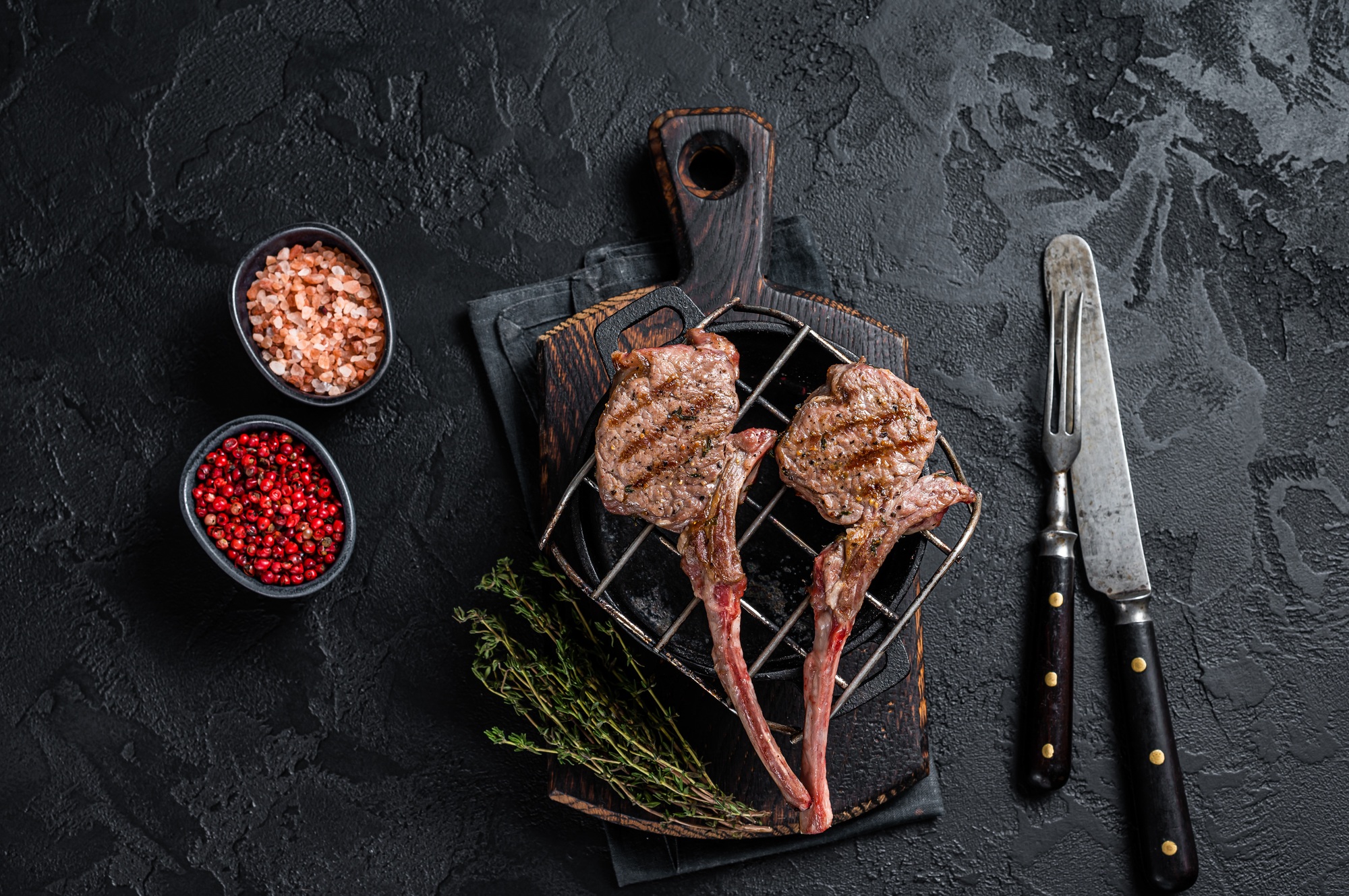 Grilled lamb mutton meat chops steaks on a grill. Black background. Top view